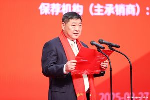 A man in front of microphone, wearing a red scarf, addressing an audience
