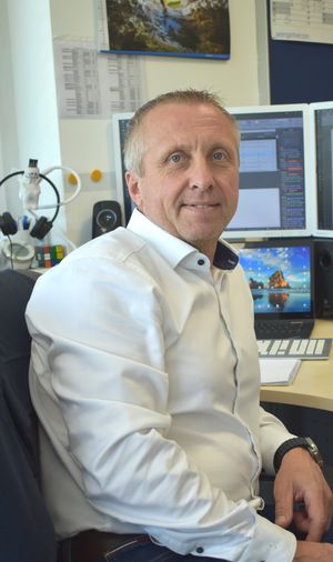 Picture of a man sitting at his desk, looking at the camera, smiling